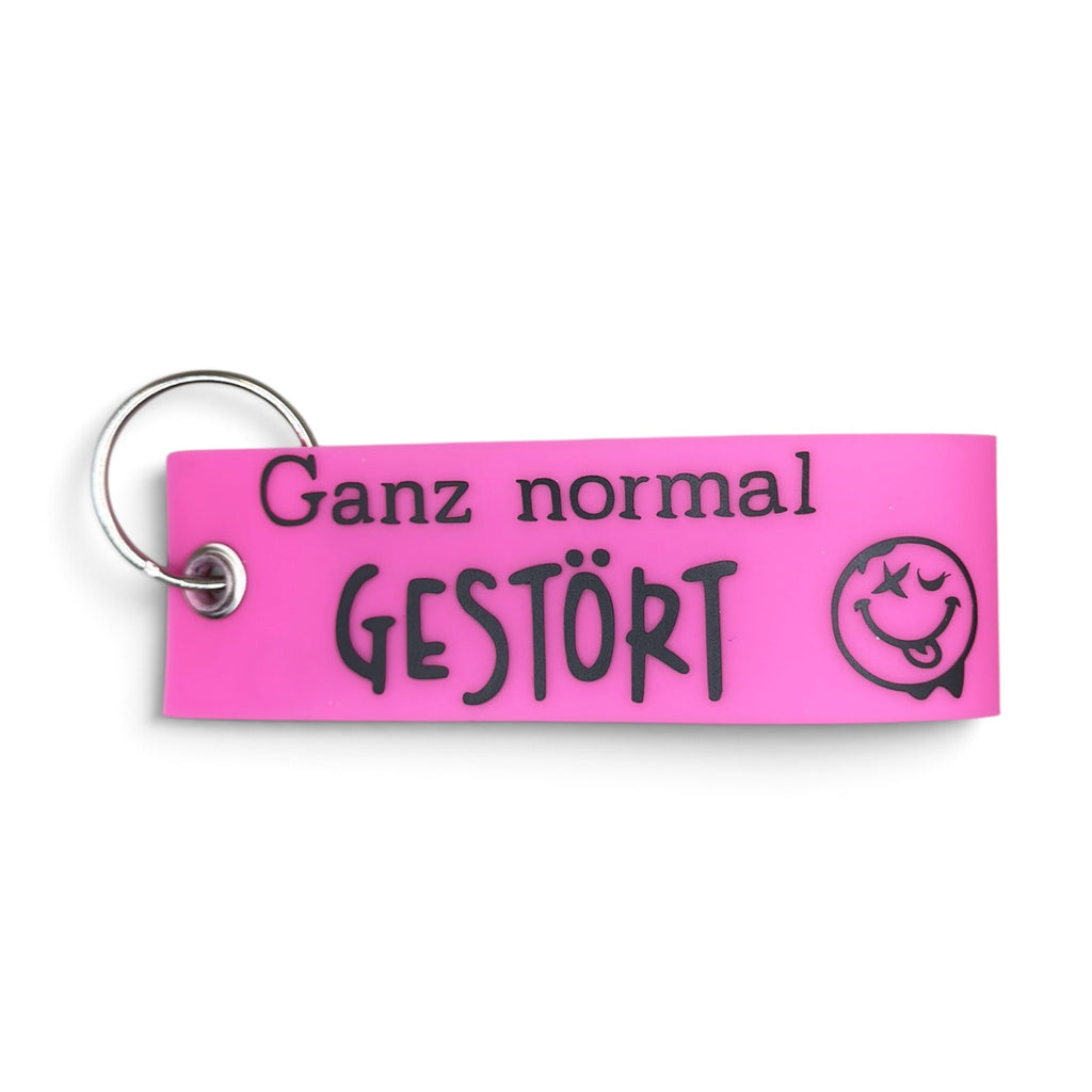 Pinker Vinyl-Schlüsselanhänger mit Aufschrift „Ganz normal gestört“ und Smiley